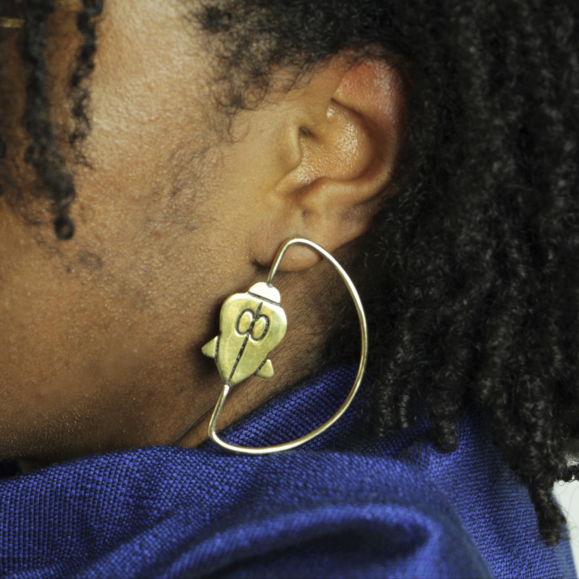Les boucles d'oreilles Ifé, création de la boutique Jelani portées par une femme avec un drapé bleu