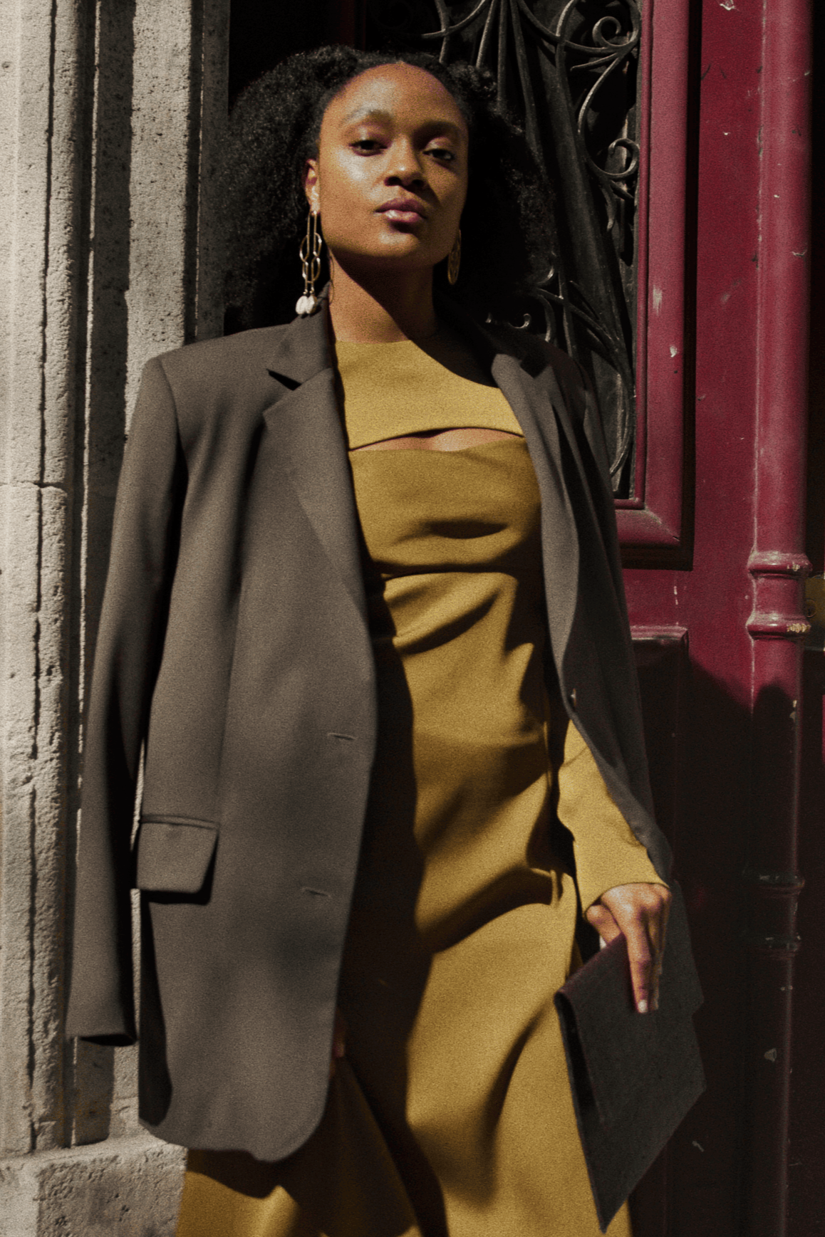Femme noire à la peau claire, pose dans la rue pour le shooting de Jelani, devant une porte bordeaux 